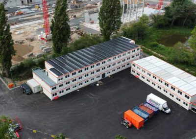 Drohnenaufnahme einer großflächigen Photovoltaikanlage auf einem modularen Büro- und Containergebäude – moderne Solarmodule zur nachhaltigen Stromerzeugung auf einer Baustelle